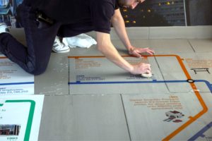 Fixing the printed floor graphics, one tile at a time, using a soft felt squeegee to push out the application fluid from under the vinyl and firmly fix the graphic onto the floor.