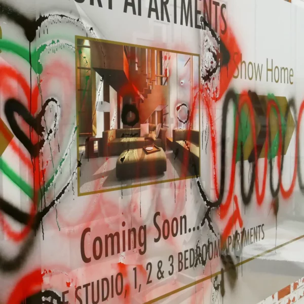Anti-graffiti laminate for protecting prints against vandalism damage and tagging, NU-COAT T27-P Satin finish film is shown covering a new homes showroom graphic on a large construction hoarding board wich is in the process of being cleaned with the appropriate spray paint cleaning agents.