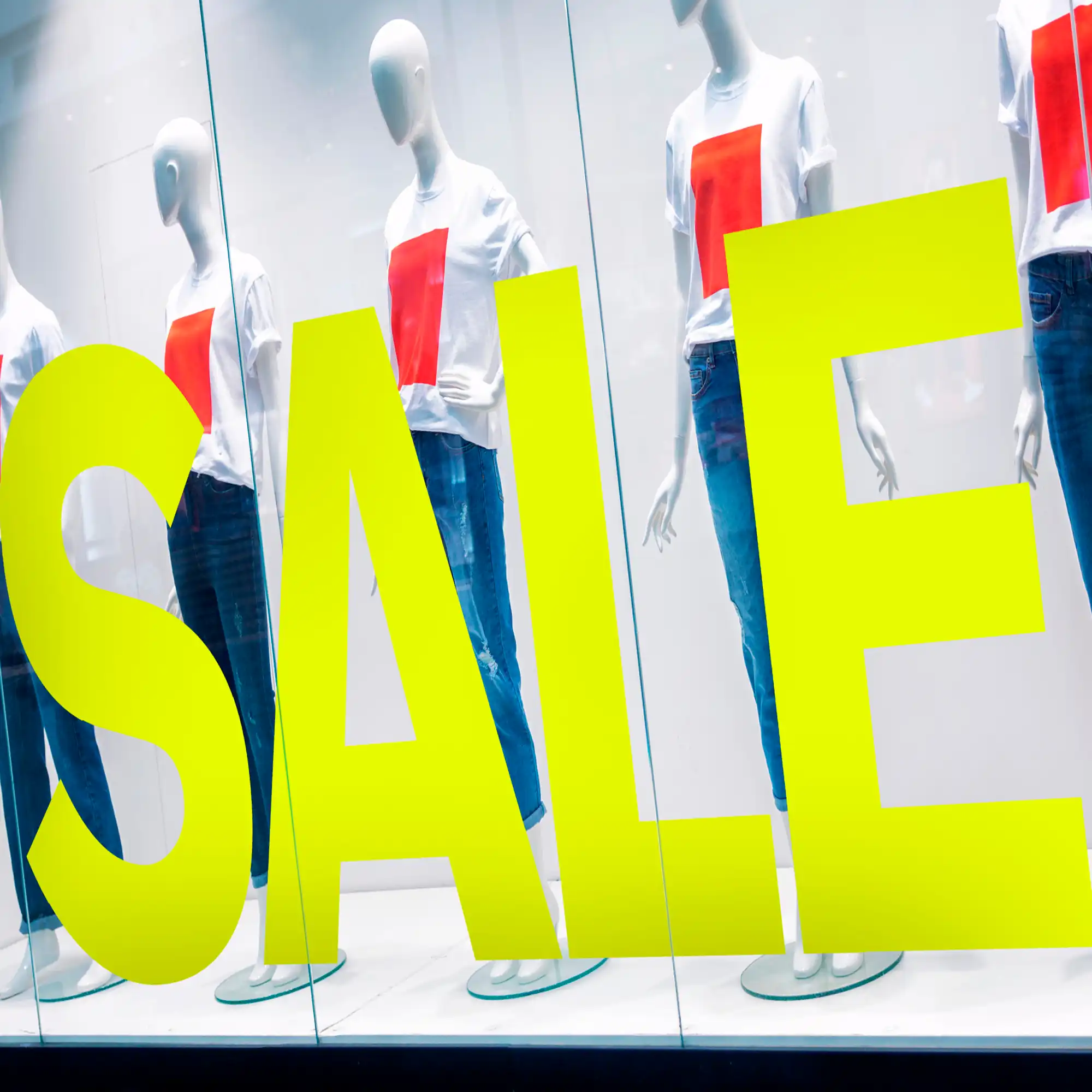 Avery Dennison 900 Fluorescent Yellow coloured cut-vinyl 'SALE' lettering applied to a clothing retailers window, advertising promotions in-store, with manaquin dummies posed in constrating, eye-catching coloured garments in the large display window behind the graphic.