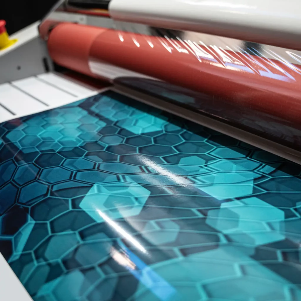 Avery Dennison DOL 2000 Series of digital print laminates, pictured in the process of being roll-fed through a wide-format roll laminator to apply the self-adhesive clear overlaminate to a printed graphic.