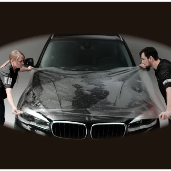 Two people stretch out a clear SPF film to cover the whole bonnet on a wide vehicle, the film is XL wide and wide enough to cover the hood with no need for seams / joins.