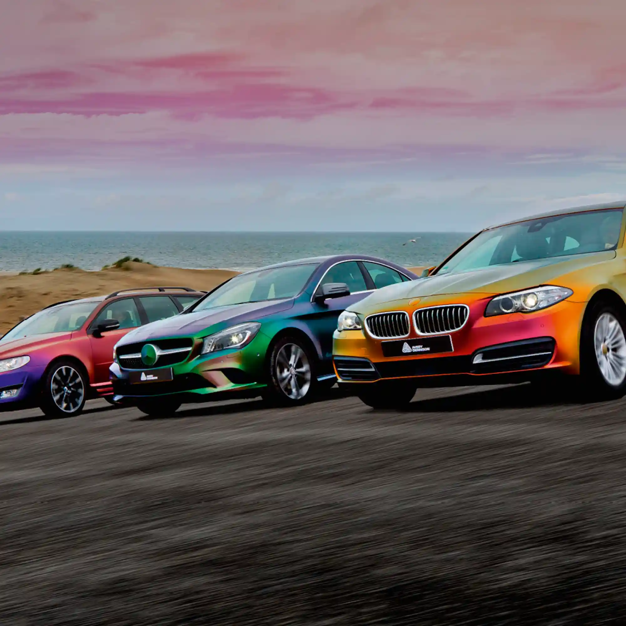 The Colorflow Series of satin, iridescent coloured vinyls from Avery Dennison's SWF range of self-adheisve colour-change films offers a stunning choice of different colours, three of the colours are shown applied fully-wrapped onto a mix of well known car models parked in a line of a beech with a purple sky in the background, the vinyl colours are from left to right: Roaring Thunder Blue/Red, Urban Jungle Silver/Green and Rising Sun Red/Gold... all offering unique, stunning visual colour effects!