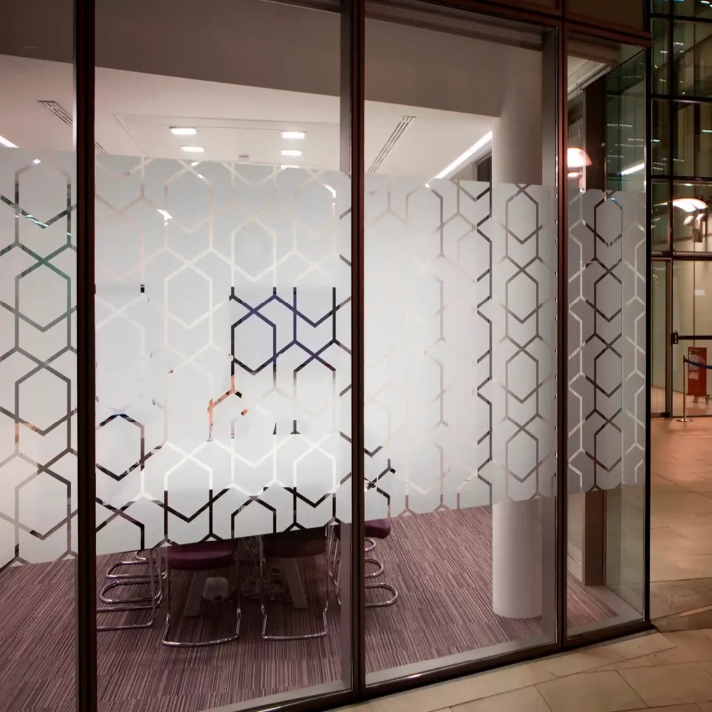 Avery Dusted decorative window film has been cut out into a symmetrical gemoetric cut-vinyl pattern to add decoration and privacy to a meeting room window, whereby you can see there are chairs and a conference table through the lower parts of the window that are not covered in vinyl and the window areas are obscured in the areas that have had the vinyl applied.