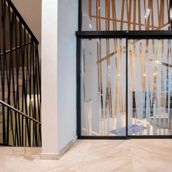 Avery Dusted self-adhesive window film with a cut-vinyl abstract shape design applied to various large office partition windows with the cutout shapes of the film matching the decorative interior of the buildings ironwork that surrounds the staircase bannisters.