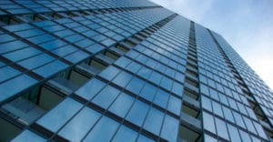 R Silver 20 Solar Control Film from Avery Dennison on an exterior office building taken from ground levele looking upward the windows tower upwards to dissapear in the blue sky at the top right of the photo.