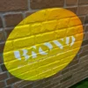 BIOND eco-friendly print film printed with a huge yellow cutout shape and renewable sustainable films text, applied onto an exterior textured brick wall.