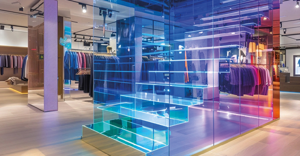 Blue dichroic self-adhesive film applied to glass panels on a retail store staircase with the final effect resembling a holographic projected image as he colour changes from blue tints into other rainbow spectrum tinted colours.
