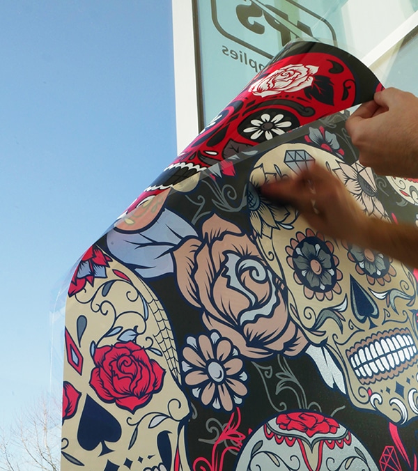 A cautionary note as a darkly printed vinyl is installed onto an external window, viewed from the inside of the glass, as the final corner is curled onto the wndow as a speedin hand squeegees it into place..