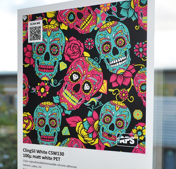 ClingSIL white window film sample media applied onto an external window with a printed graphic of a multitude of skulls and roses in vivid magenta, yellow and aqua colours on a black background.