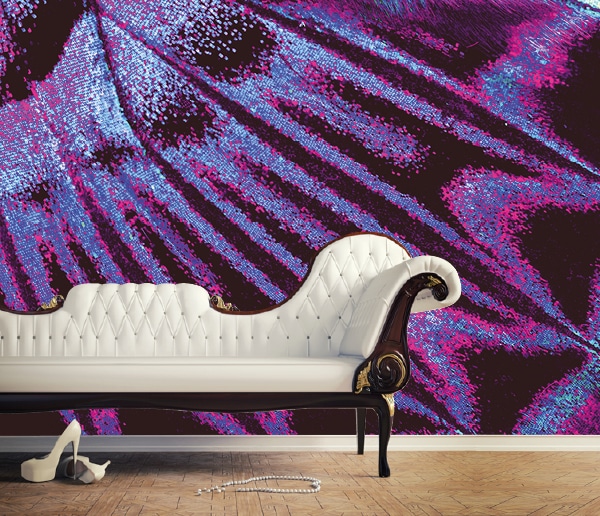 DEKORA bespoke wide-format printable interior decoration wallpaper has been custom printed with a purple, cyan and magenta close up image of a butterfly wing, hung on a living room wall with a couch in front.