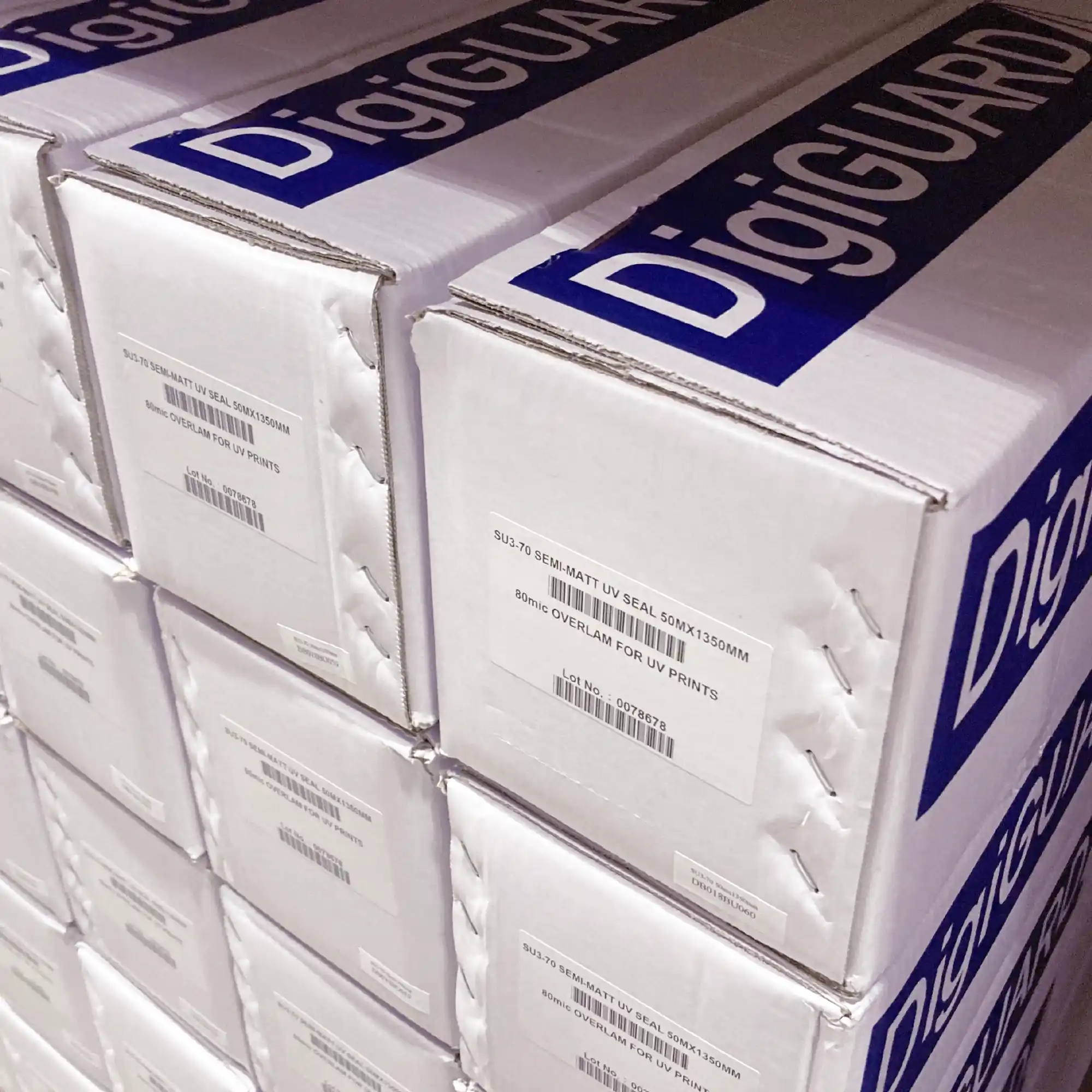 Fire-rated, semi-matt printers laminate, DigiGuard SU3-70 for protection of UV digital prints and self-adhesive signage is pictured in branded packaging boxes, stacked tidily on a warehouse shelf.