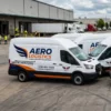 Fleet of white commercial vans with professionally printed branded vehicle graphics, parked outside a logistics warehouse.