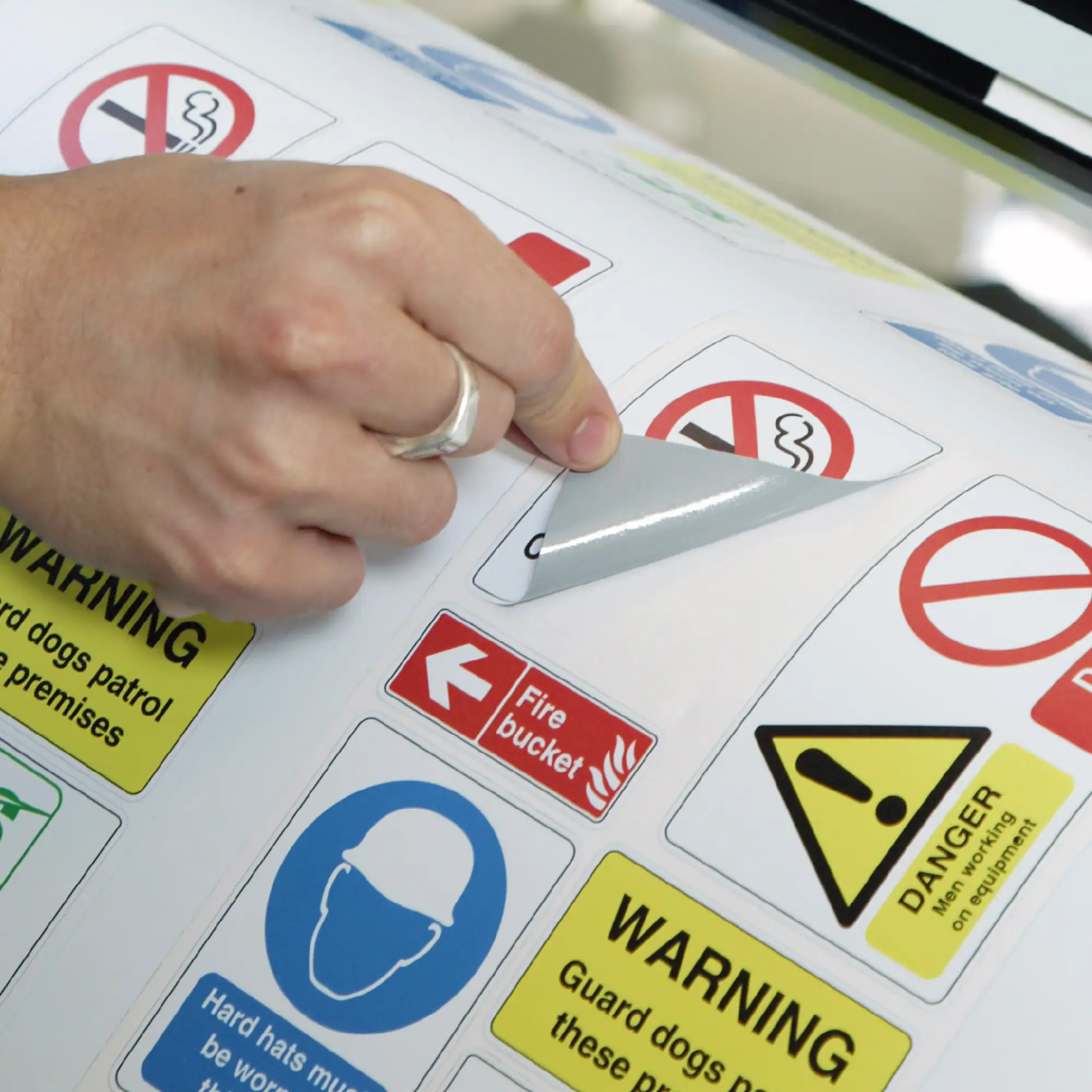 DigiPRINT DS3005 textured, thick print n cut label vinyl printed in imposed rows woth an assortment of different safety labels with a focus on a no nsmoking sticker which is being peeled back from the release liner with all the waste film that is not required around the kiss-cut graphic has been weeded out / removed.