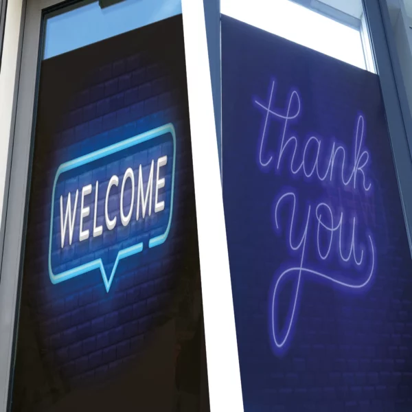 Showing two photos side-by-side, a glass office buildings' entrance door features a professional looking printed image using self-adhesive, DigiPRINT DS3047 double-sided blockout window graphics vinyl. On the outside, bold white lettering on a clean, dark background reads “Welcome,” in a neon styled printed graphic that invites customers in with a friendly, polished appearance. From the inside, the reverse side of the graphic displays a matching “Thank You” message, visible as patrons exit. The blockout vinyl ensures no light passes through, maintaining full opacity and vibrant readability from both sides. The print is crisp and smooth, seamlessly applied to the glass, giving the door a high-quality, branded finish from both sides.
