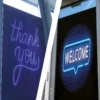 Showing two photos side-by-side, an offices entrance door features a self-adhesive double-sided window print vinyl with a black blockout layer and removable adhesive, DigiPRINT DS3049. On the outside, bold white lettering in a neon styled typeface is printed on a clean, dark background reading “Welcome” to invite guests in with a friendly, professional appearance. From the inside, the reverse side of the graphic shows a “Thank You” message that is visible as patrons exit. This black blockout vinyl ensures no light passes through the print to maintain full opacity and vibrant readability when viewed from either siode of the film. The print is crisp and clear and is applied seamlessly to the glass, providing the glass door with a high-quality, branded finish viewable from both sides.