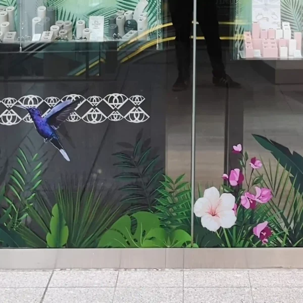A full-color print using DigiPrint DS3054P permanent ultra-clear window film applied onto a glass store-front window with graphics of bright tropical birds and vibrant jungle foliage that creates a high-impact visual without obstructing natural light of the view through the glass into the store behind. The ultra-clear PVC film offers a good alternaive to clear polyester films when applying onto glass and allows for a clean, seamless 'no vinyl' look, making the print appear as if it’s directly embedded into the glass. Designed for display prints onto glass surfaces, the permanent self-adhesive secures the graphic in place and the clarity of the vinyl is perfect for retail branding and decorative installations on windows.