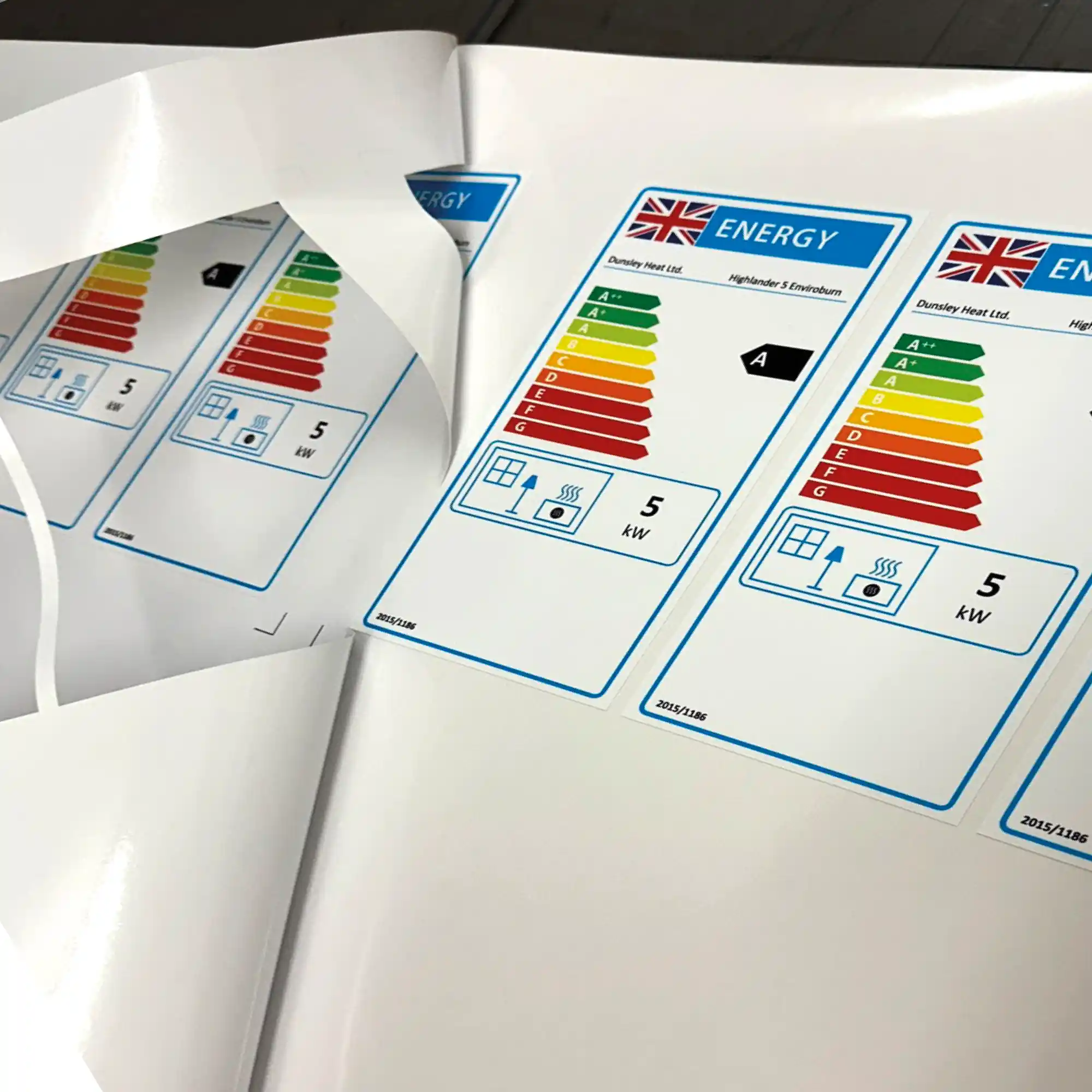 DigiPRINT monomeric series of thick print vinyls are ideal self-adhesive print films for producing cut labels and stickers. DS3007 gloss white film is shown printed with energy labels, often found on electronics packaging, and the printed roll is laid on a table shown in the process of being weeded out / the excess unwanted film that surrounds the printed graphic being peeled back and removed.