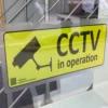 Printed on DigiPRINT PrintDOT Matt Clear film, a bright yellow and black 'CCTV in operation' sign is stuck on the inside of an external office front window. The special, easy to apply, DOT PATTERN adhesive is just visible as the reverse printed graphic has been stuck to the inside of the glass window surface.