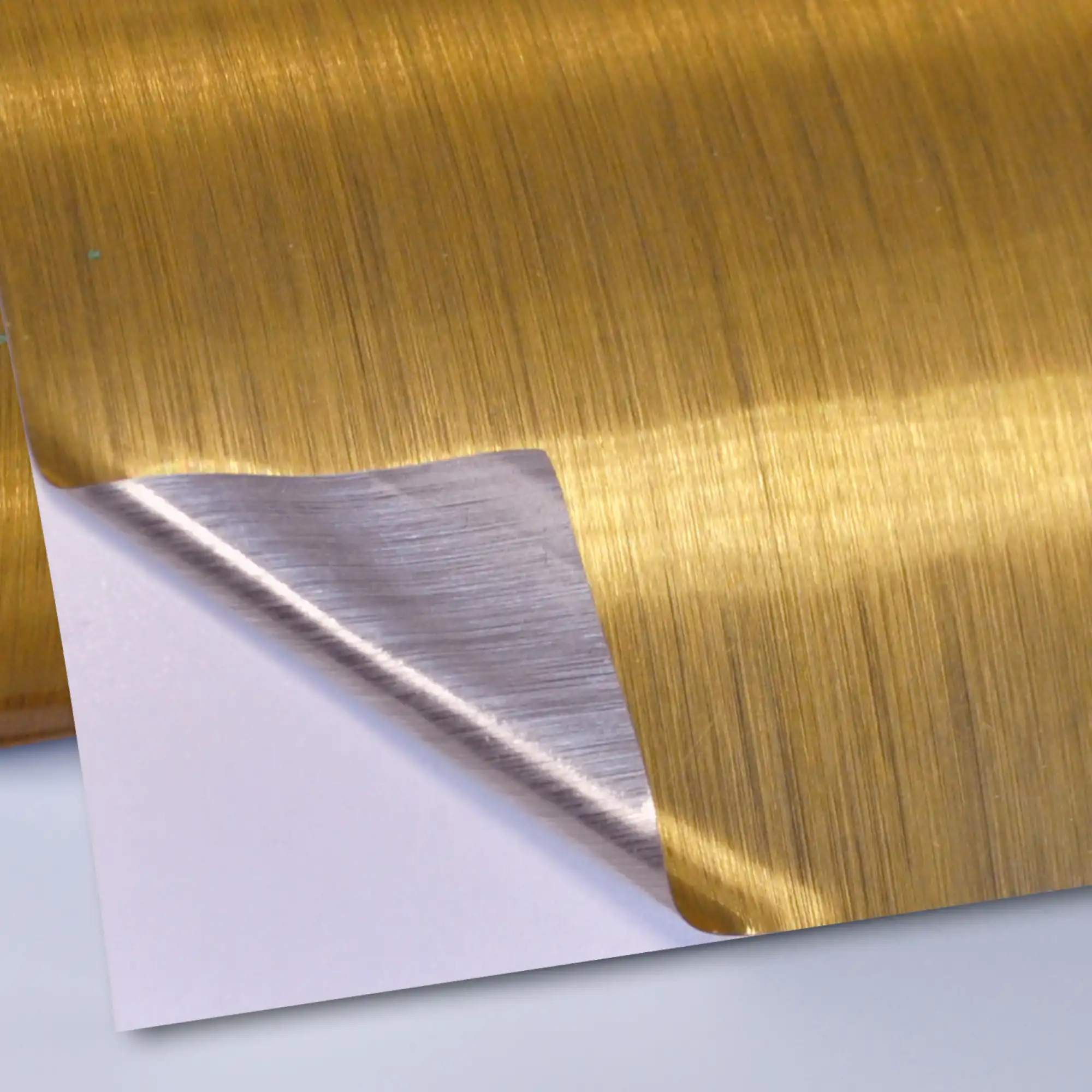 DigiPRINT TSBG3 brushed gold one-way viewable metallised print film on a roll showing the eye catching gold brushed effect metal of the face film with one corner edge folded over to show the silver on the adhesive side as it is pulled away from the liner.
