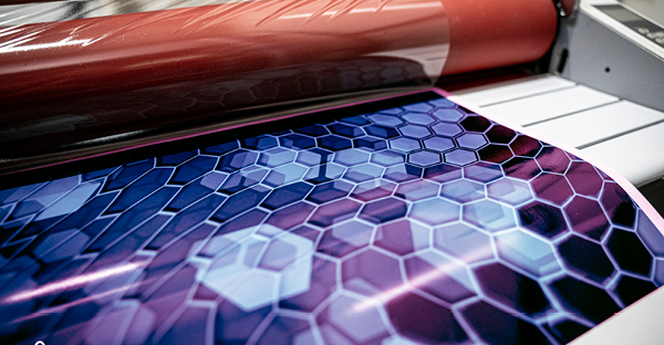 DOL 2480 gloss digital print laminate for applications onto curved surfaces and longer term protection of printed graphics is shown here being applied to a wide-format printed image on a roll-fed laminator.