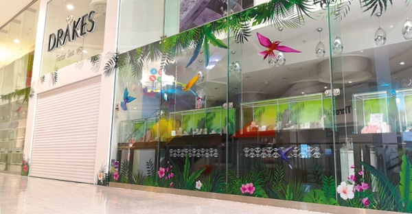 A retail shop front store window with DS3054 optically clear print vinyl printed with a beautifully tropical scene of flying birds and fauna surrounding the glass window display. 