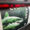 EventSharK, from Kernow Coatings, on a wide format digital printer, printing a promotional floor graphic showing a green stylised shark and waves background.