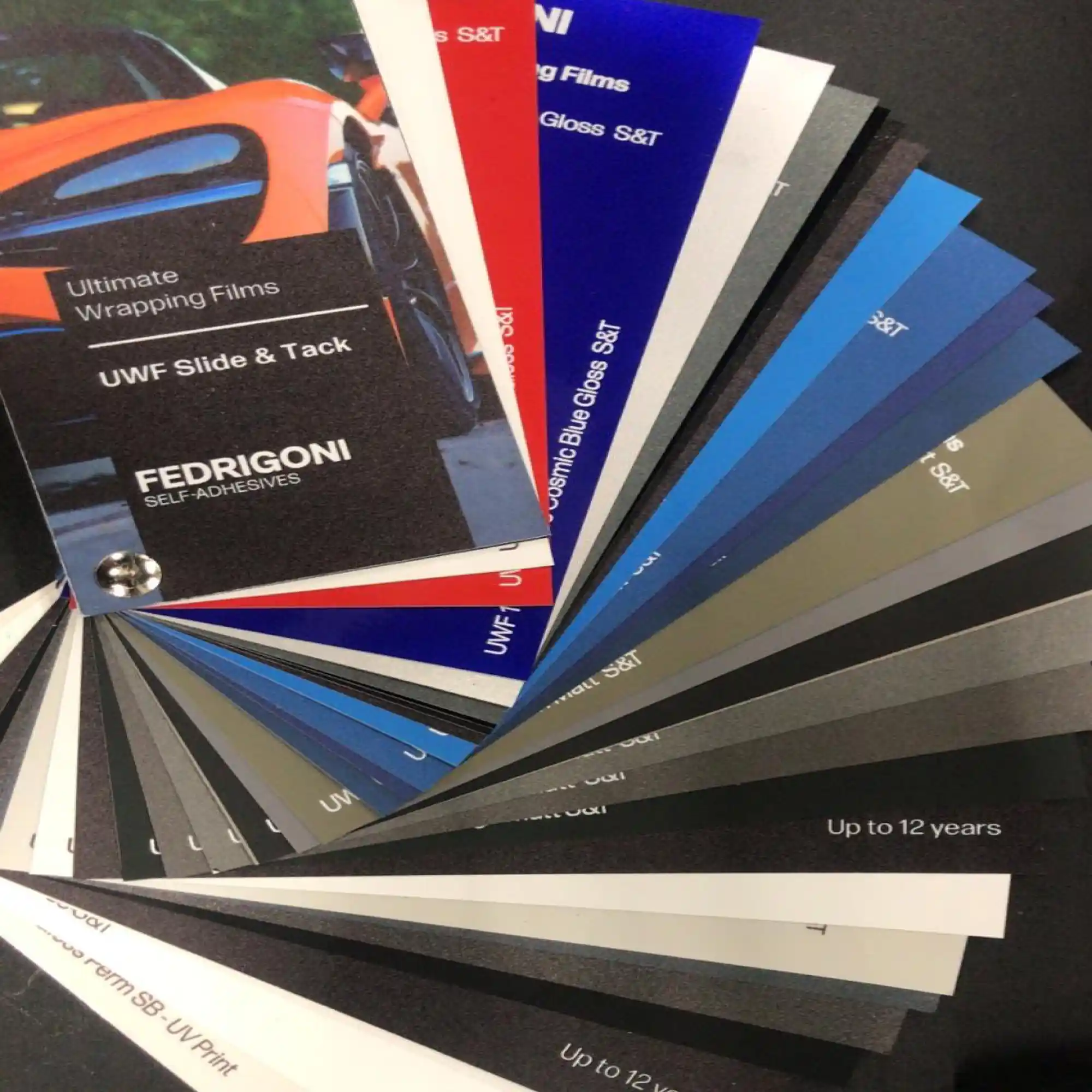 The Fedrigoni Ultimate Wrapping Films (UWF) range of colour vehicle wrap vinyls swatch is fanned out to show the current range of conformable cast colour films.