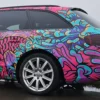 Fedrigoni C30 gloss vehicle wrap laminate on the C50 printed film, both fully wrapped onto this Audi car of a brightly printed fish and fauna red, purple and green with black outlines design, showing close-up on the rear side detail of the cars contours, around wheel trim, rear light and door handles.