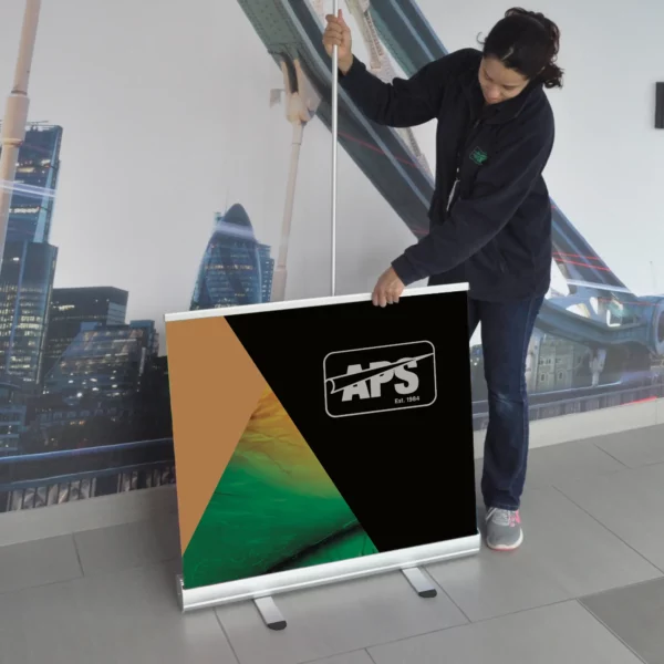 Pulling up the printed roll-up display banner graphic with it extended half-way showing the support pole behind and the cassette and 2 x extended feet at the bottom of the photo.