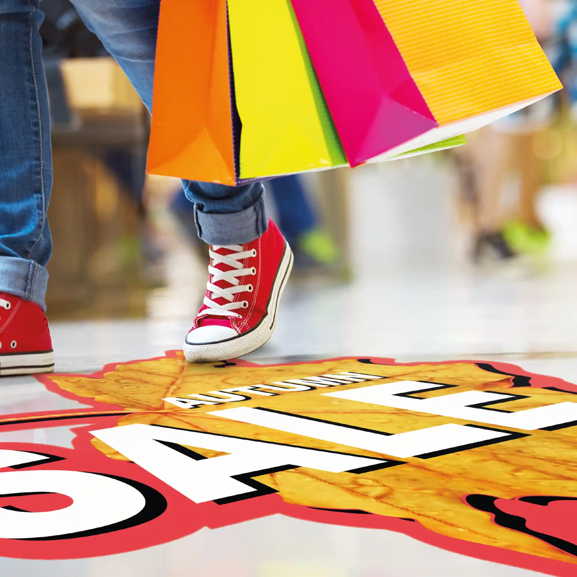 DigiGUARD GUARDIAN Prop12 floor graphic laminate protecting a printed autumn sale flooring sticker as a young lady holding 3 colourful and bright shopping bags walks over the promotional floor print in a shopping centre.