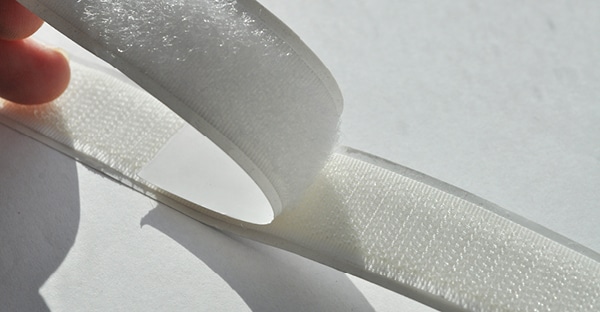 A photo close-up of the white strips of both the hook and the loop sign tape being stuck together to show the two different adhering sides of the tapes more clearly... the hook side is on top and the loop side underneath.
