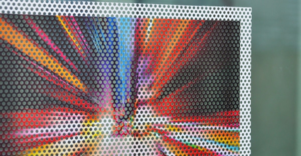 JT5817 PUV one-way vision perforated window film close-up photo of a light explosion printed image in a spectrum of reds, oranges, yellow and blues. You can clearly see the hole to vinyl ratio of the perforations in the film which allow the light through while still showing a great view of the colourful graphic.