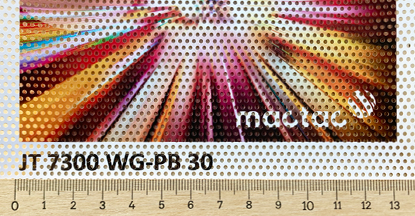 A close-up view of Mactac JT 7300 WG-PB 30 one-way vision window film, viewed straight on with a printed image to detail the hole-to-vinyl ratio and printed image quality, with a ruler beneath to illustrate the actual physical hole/vinyl sizes.