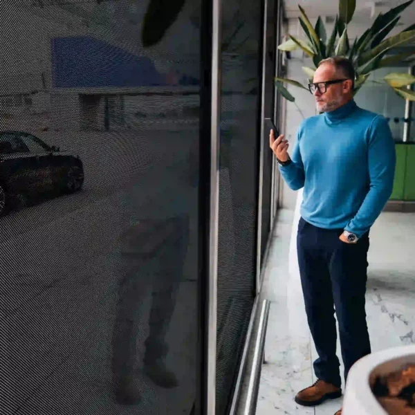Mactac JT 7300 WG-PB 40, 60-40 vinyl to hole ratio one way vision window privacy film applied onto a large street store window as seen from the inside looking outwards onto the street outside which is visible, but anyone looking in cannot see the man inside on his phone as he looks at his mobile phone.