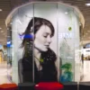 Mactac JT 9500 CG-RT clear transparent gloss removable adhesive printed graphics vinyl applied to a glass booth advertising display in a shopping precinct.