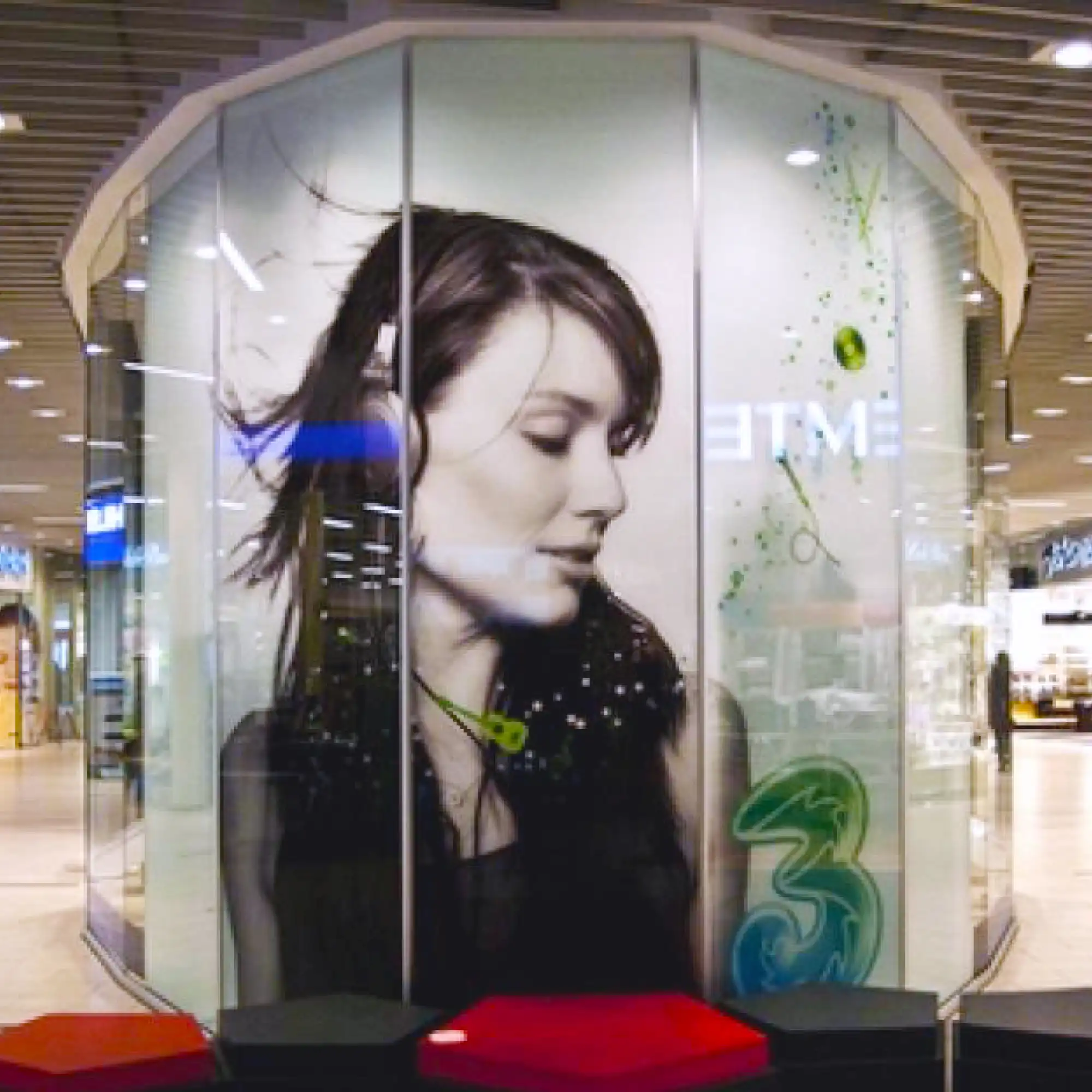 Mactac JT 9500 CG-RT clear transparent gloss removable adhesive printed graphics vinyl applied to a glass booth advertising display in a shopping precinct.