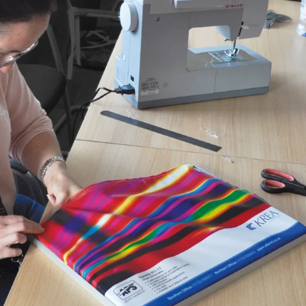 Keder Lip PVC stitch-on tape, having been sewn around all four edges of a printed textile graphic, is being inserted into the edges of an alluminium tension display frame