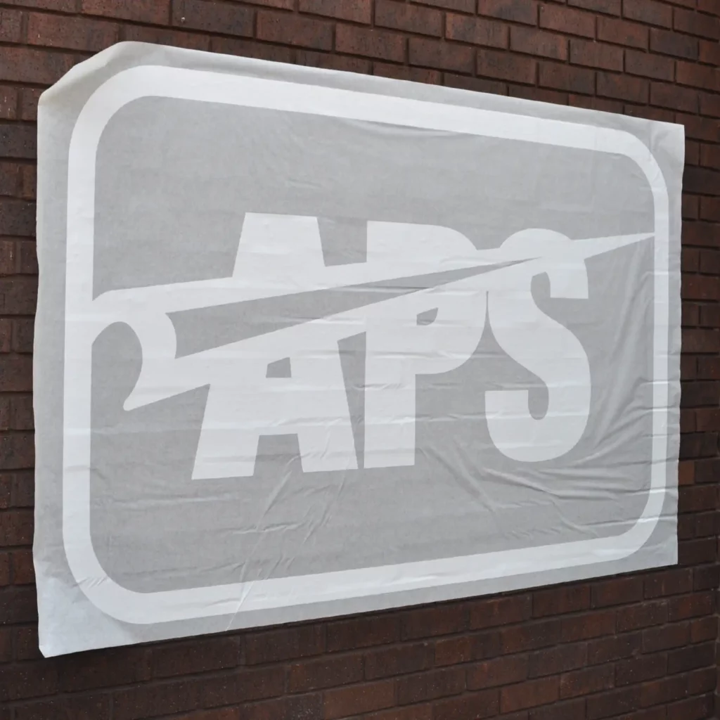 Self-adhesive graphics transfer paper for sign vinyls seen here holding a cut-out logo graphic in position over a brick wall prior to the app tape being reoved leaving the flogo graphic applied to the surface and perfectly positioned.