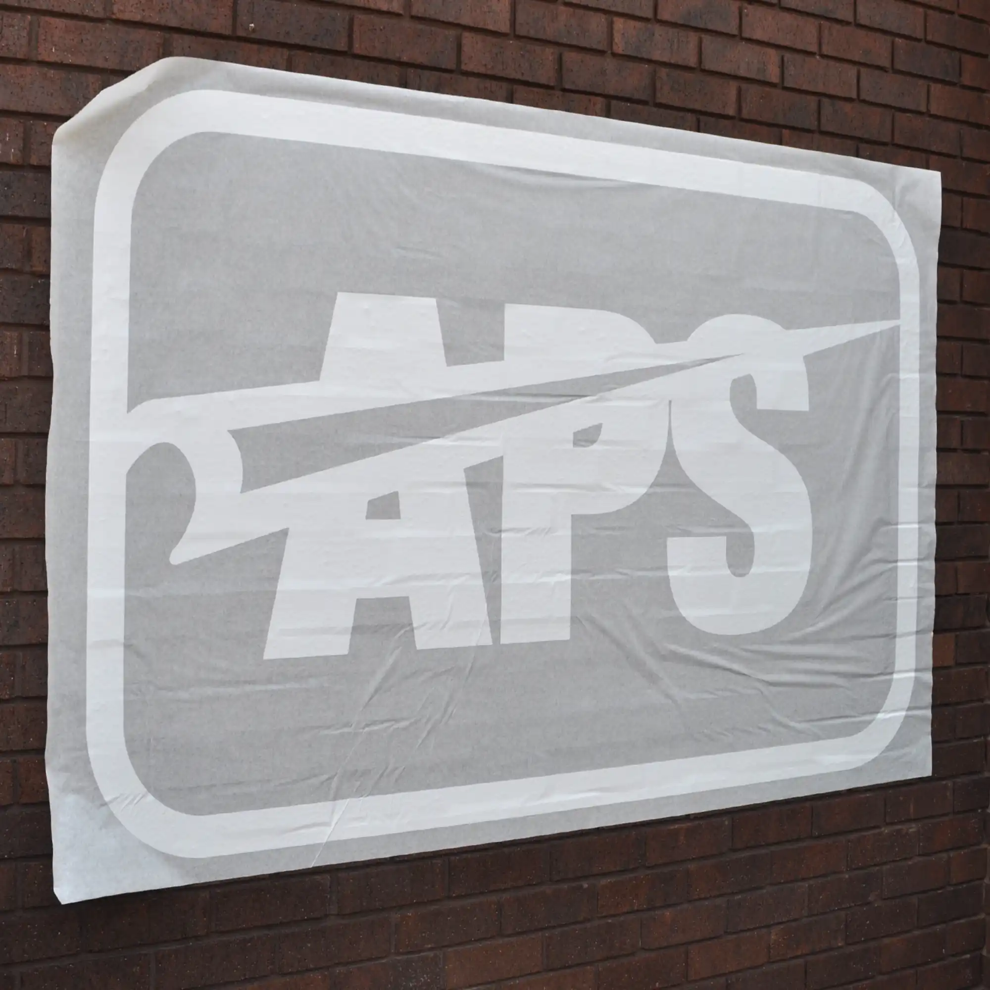 Self-adhesive graphics transfer paper for sign vinyls seen here holding a cut-out logo graphic in position over a brick wall prior to the app tape being reoved leaving the flogo graphic applied to the surface and perfectly positioned.