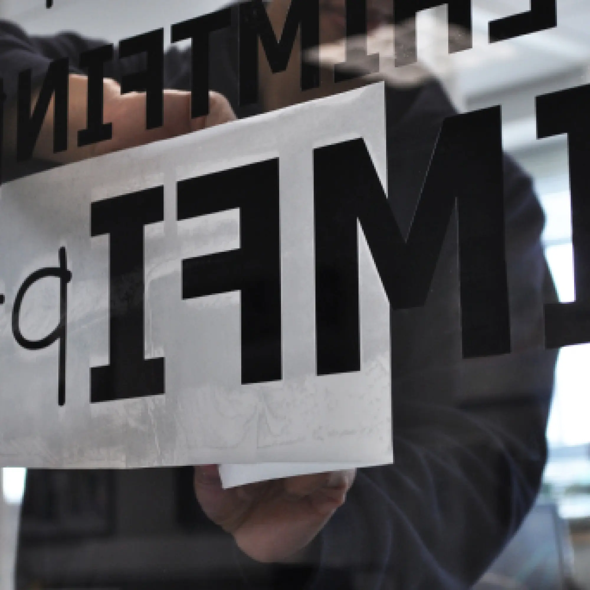 Transfering black cut vinyl lettering onto an internal window viewed through the glass you can see the application tape being peeled back and exposing the letters, as viewed from the adhesive side of the transfer paper.