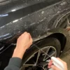 Lifting an edge of Paint Protection FIlm and spraying a slide solution underneath the film to position the film onto a car wheel arch area.