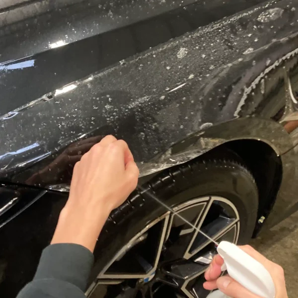 Lifting an edge of Paint Protection FIlm and spraying a slide solution underneath the film to position the film onto a car wheel arch area.