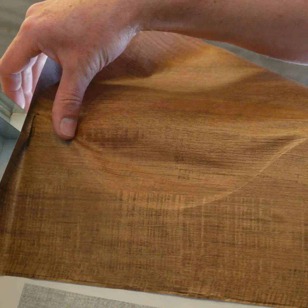 Shaping some real wood effect vinyl interior film into a contour shaped surface using finesse, fingers and use of a little heat from a heat-gun.