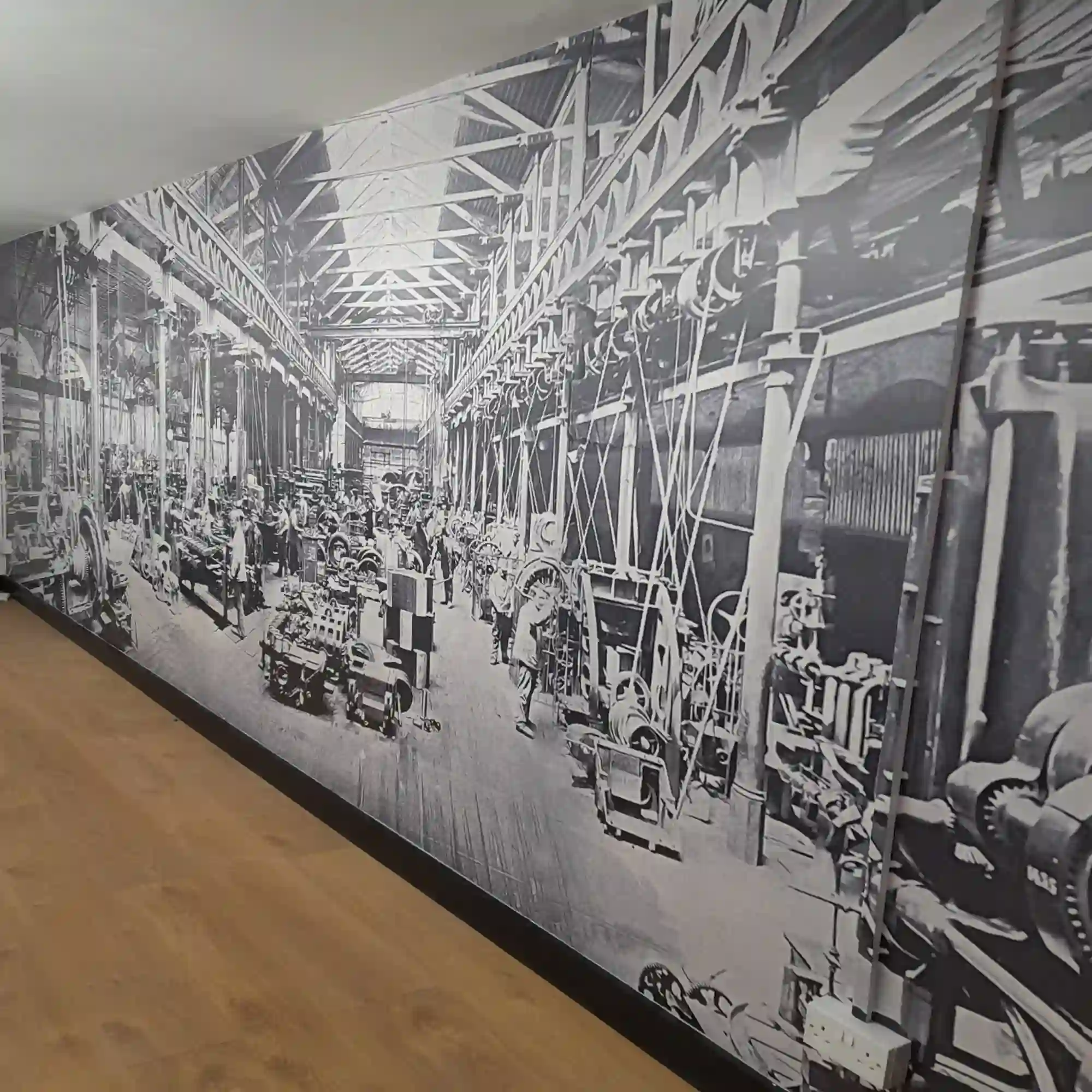 NU-COAT M12-H high opacity print vinyl with a high grab self-adhesive is perfect for applications like the picture shows here, where a black and white print of a historical photo is applied to an interior office wall, depicting a factory floor and industry from a past era.