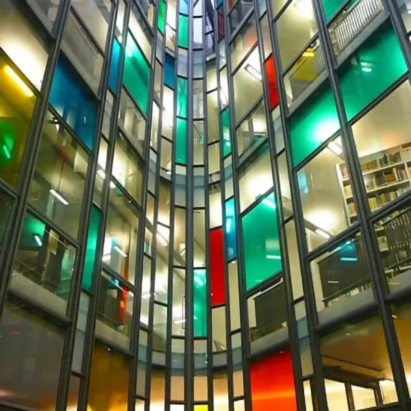Mactac MACcrystal 8400 Series coloured window films in an abstract pattern of green, red and blue transparent tints applied to the glass windows on all floors in this office atrium, viewed from ground level and looing up, the dark grey edges of the glazing frame the coloured windows and make a striking, elegant and eye-catching colourful display.