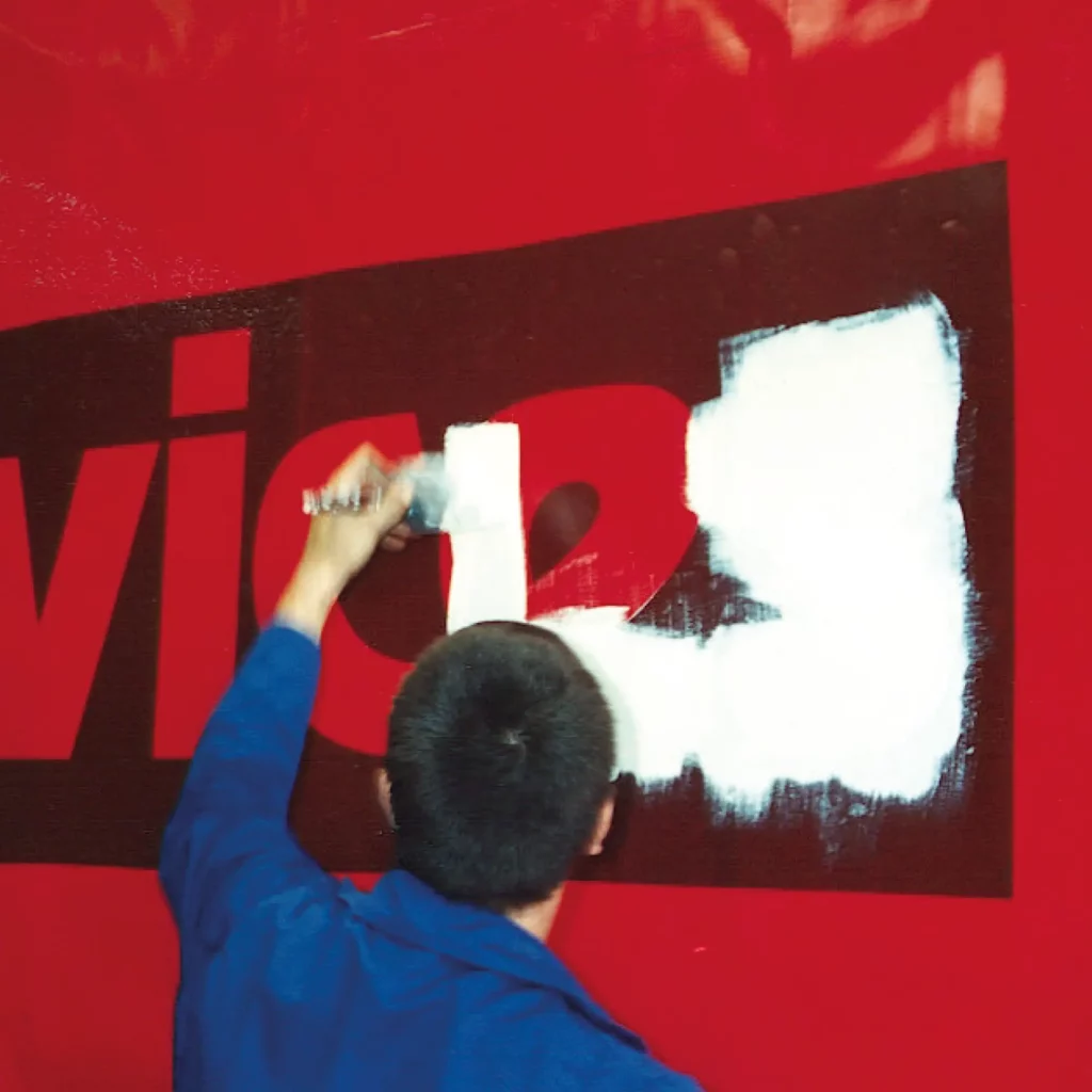 The self-adhesive stencil graphic has been applied to the surface of this large trucks red curtain side and is being painted over with the stencil acting as a mask for the graphic so the pain only touches the red curtain side of the vehicle and when the stencil is removed after the paint has dried, a clean, crisp stenciled image is all that is left in place.