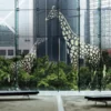 Mactac 700 Tint coloured graphics vinyl has been applied to a very large lobby window using cut-vinyl shapes to create the image of a young Giraffe looking up at a larger parent Giraffe providing a light and airy window decoration with low shrubbery on the outside of the room providing an organic feel to the finished interior space.