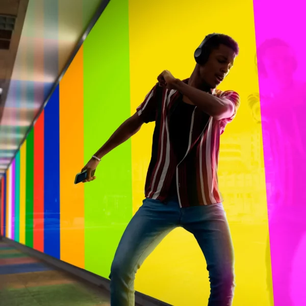 Mactac 9700 Series of transparent coloured lightbox films are placed side-by-side in complimentary colour stripes to create a decorative and brightly coloured backlit window display with a funky dude listening to music on headphones, dancing in front and his reflection just about visible in the glass.