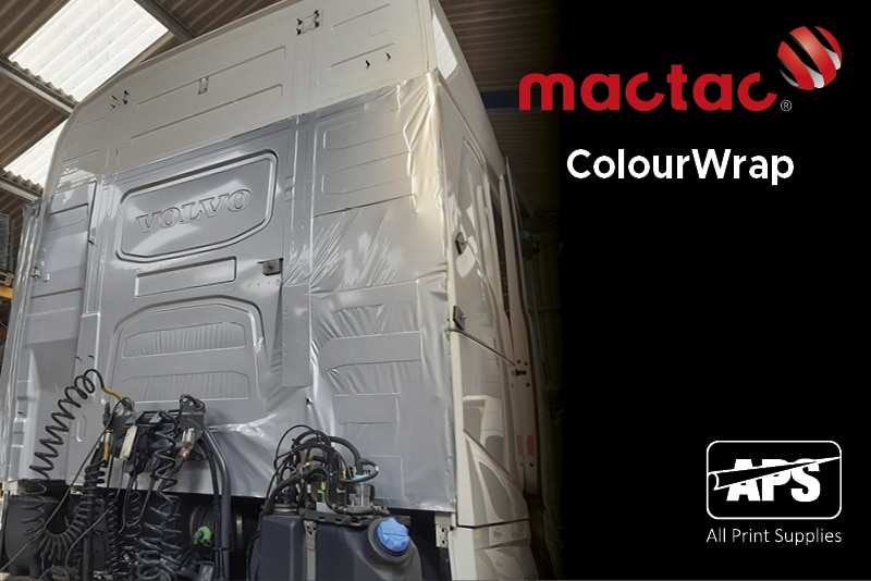 Mactac ColourWrap GM61 gloss metallic silver CAD wrapping film in the process of being applied to wrap the entire truck cabin of a Volvo Truck and is halfway through being applied into the contours of the deeply recessed areas at the back of the cab with the indented Volvo logo prominent and a higly visible feature.
