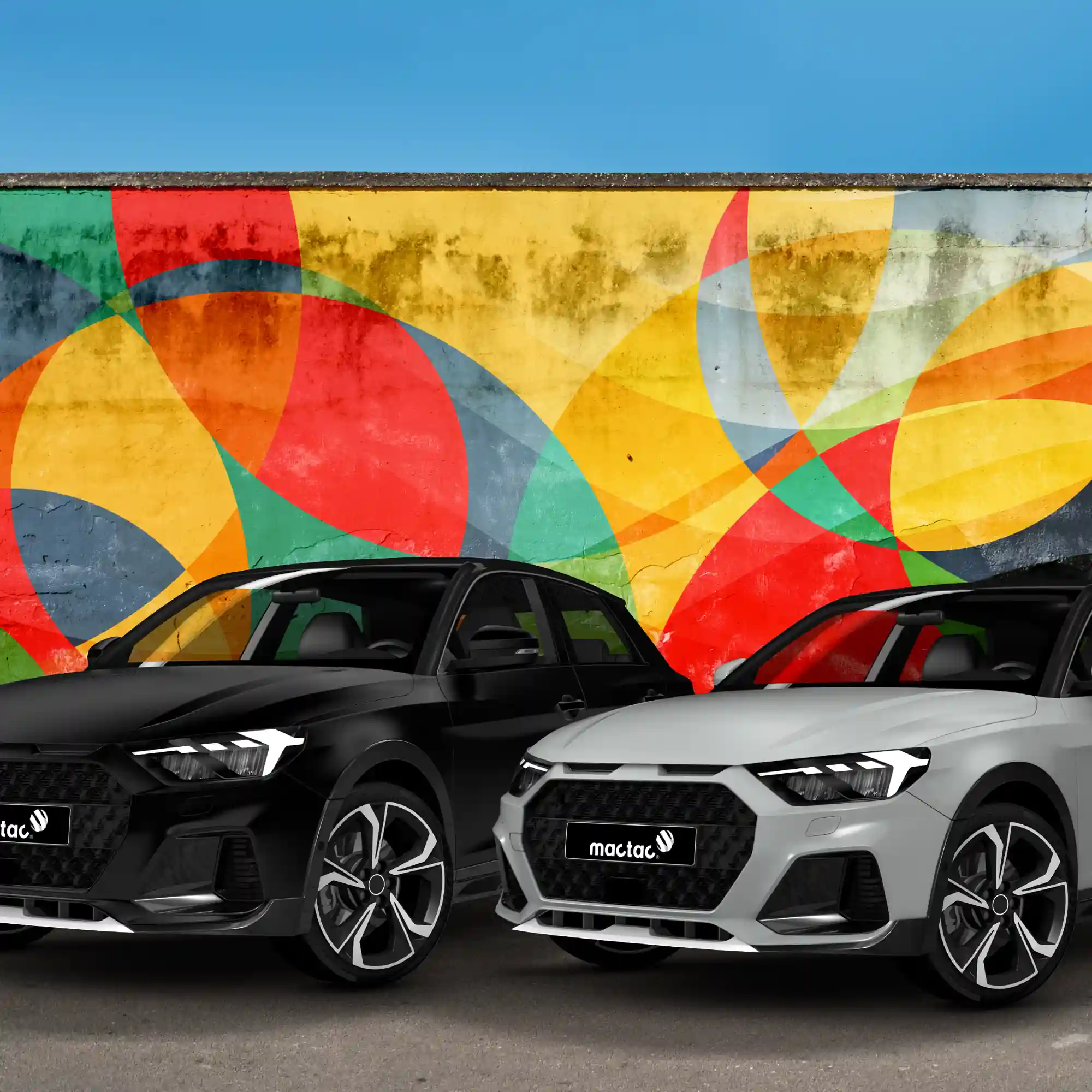 Mactac Colourwrap Series of coloured gloss and matt vehicle wrapping films offer a wide choice of different vinyl colours for car wraps, with the grey and black vinyl options shown here applied to 2 modern road cars which have parked with front wheels turned slightly, in unison, in front of an abstract patterned wall graphic with a perfect blue sky above.